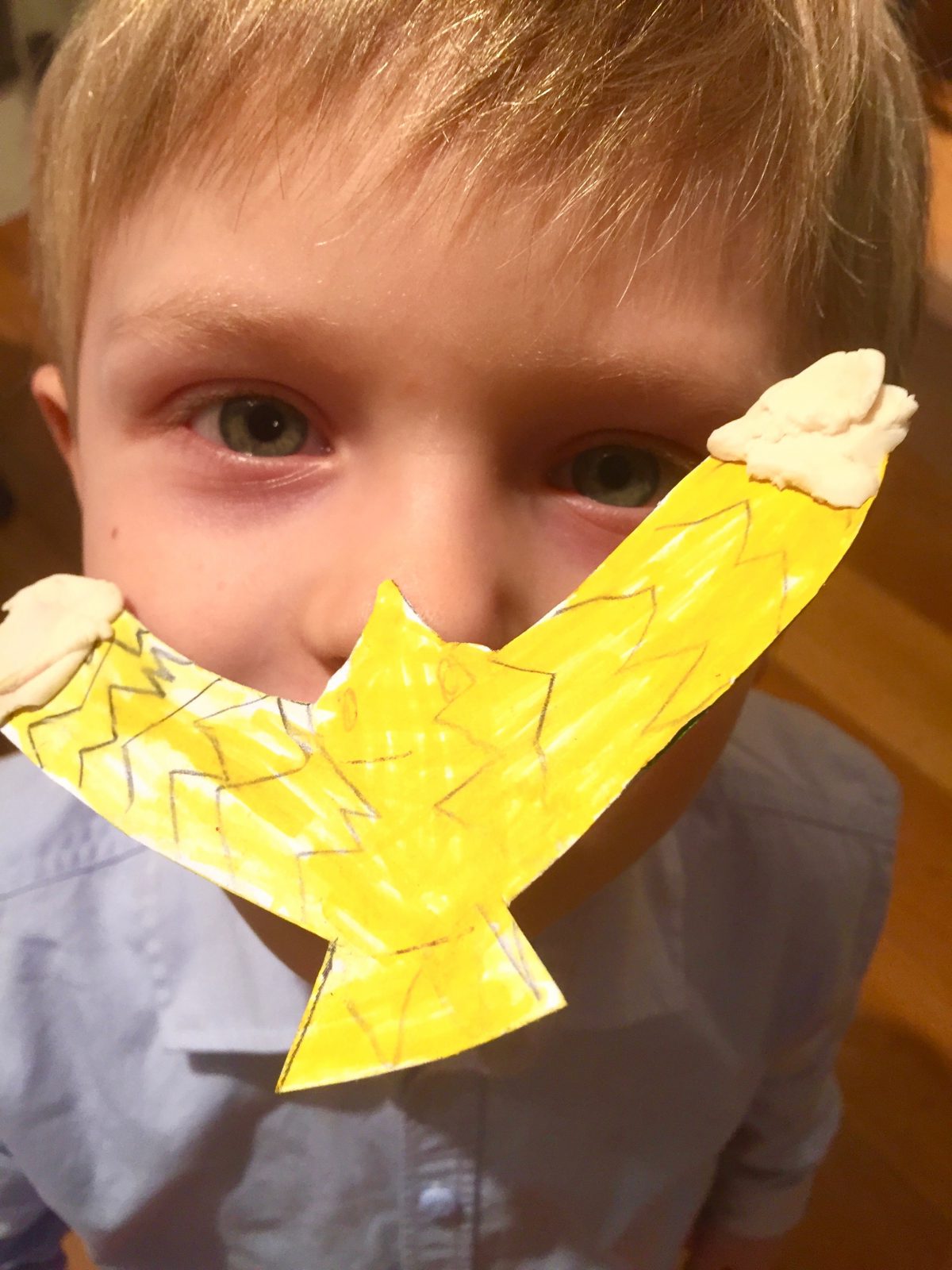 Ein gebastelter Zaubervogel, gelb bemalt, schwebt auf der Nase eines Kindes.