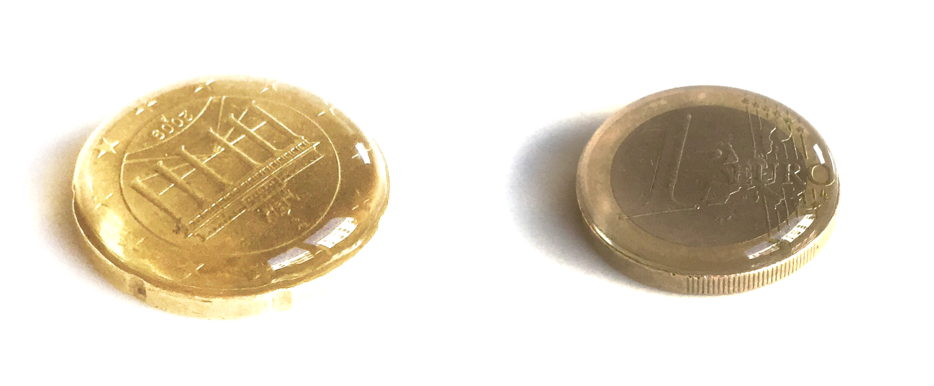 Zu sehen sind zwei Geldmünzen. Links die Rückseite einer 50 Cent-Münze, rechts die Front einer 1 Euro-Münze. Auf beiden ist Wasser gefüllt, das einen kleinen Wasserberg bildet, aber nicht überläuft.